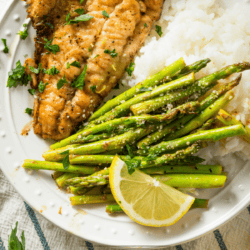 Overhead image of sauteed asparagus and chicken breast on a white plate with rice