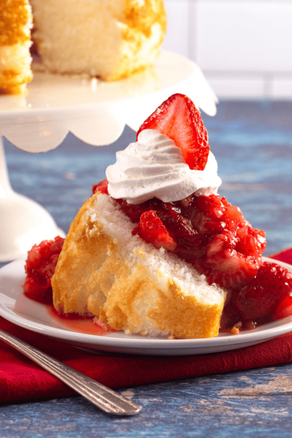 Strawberry Angel Food Cake on a plate with a cake stand of cake in the background