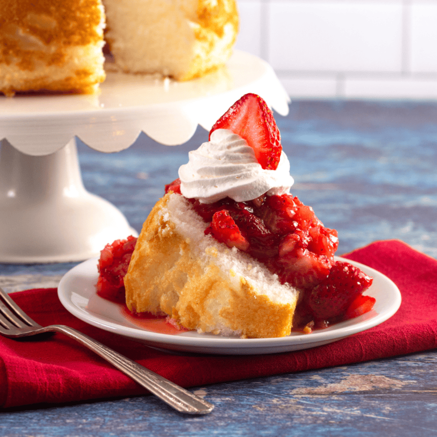 Strawberry Angel Food Cake on a plate with a cake stand of cake in the background