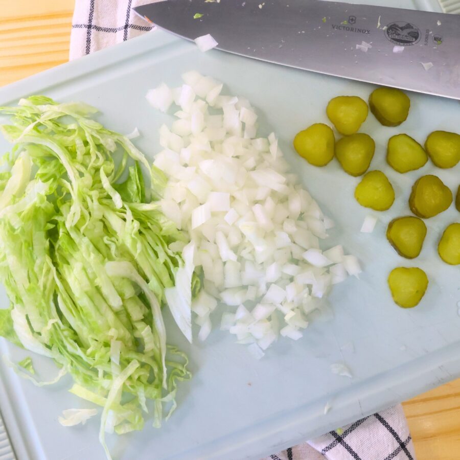 Lettuce, pickles, and onions on a cutting board with a knife