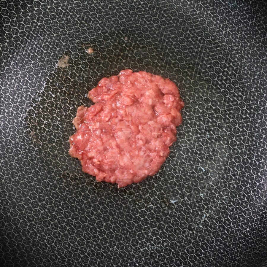 A hamburger patty cooking in a skillet