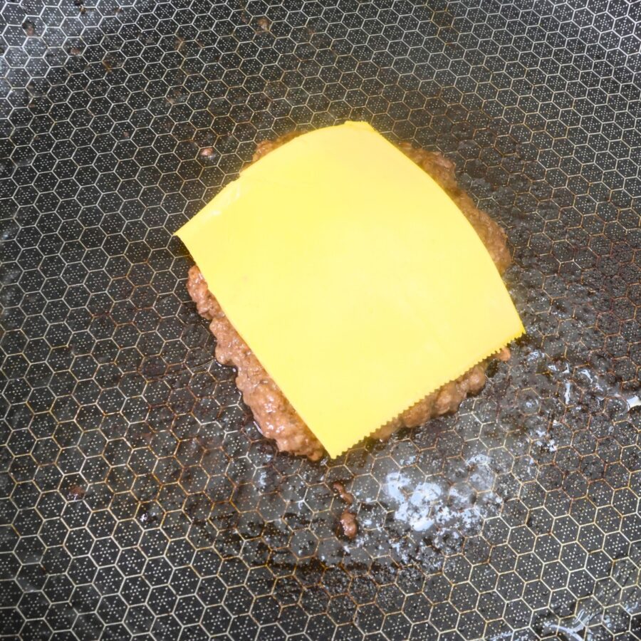 Cooked ground beef patty with a slice of American cheese on top in a skillet