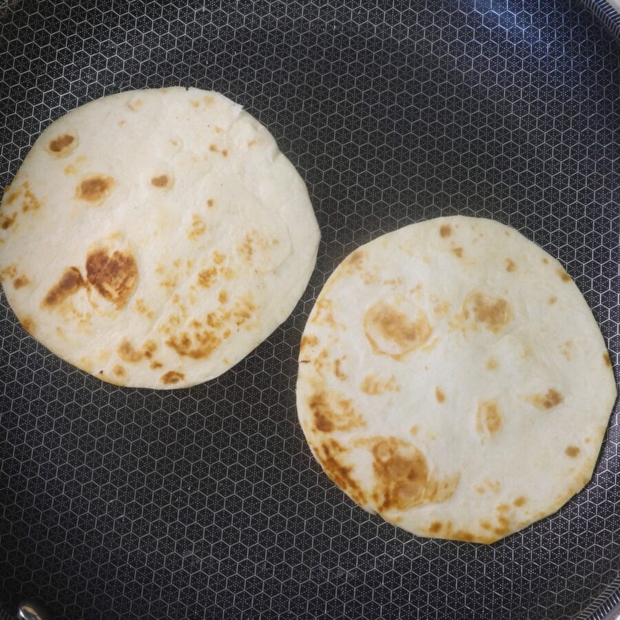 Two small flour tortillas being toasted in a skillet