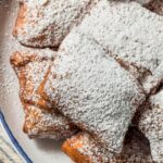Overhead image of beignets dusted with powdered sugar on a plate