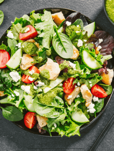 Overhead image of a beautiful spinach salad with a side of pesto dressing