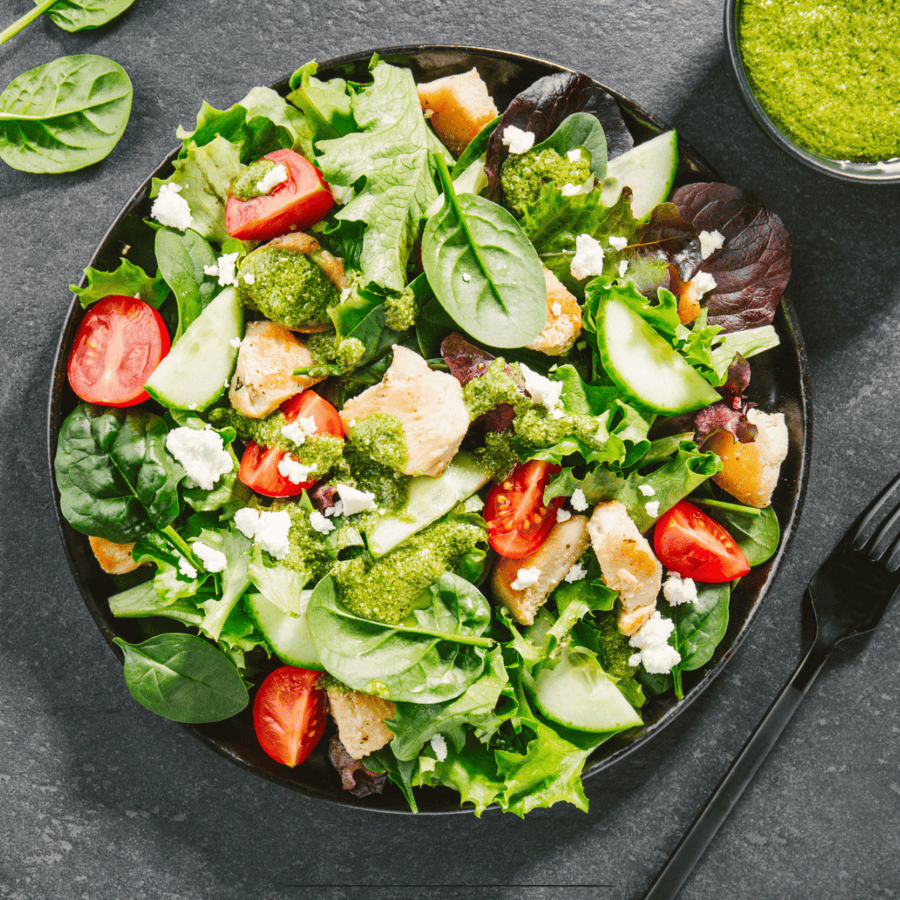 Overhead image of a beautiful spinach salad with a side of pesto dressing