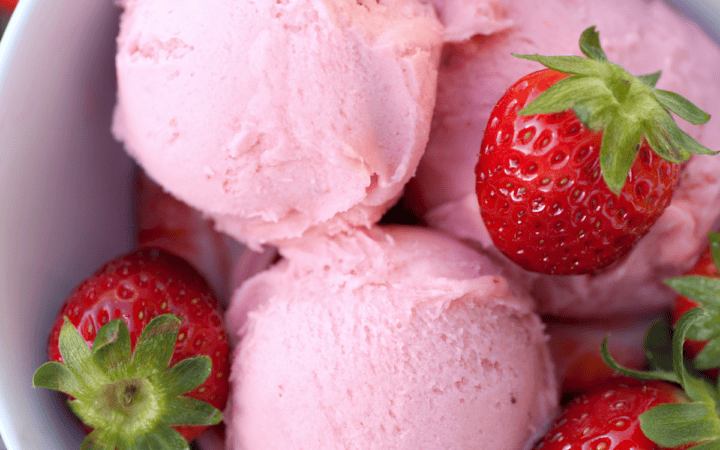 Close up image of strawberry ice cream and strawberries in a white bowl