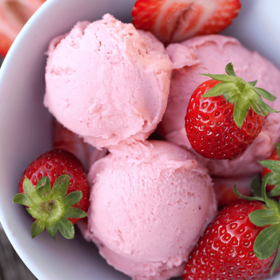 Close up image of strawberry ice cream and strawberries in a white bowl