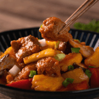 sweet and sour pork in a black bowl with chopsticks