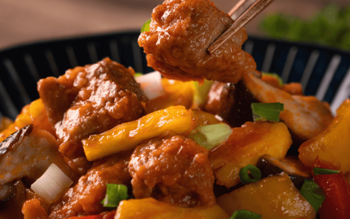 sweet and sour pork in a black bowl with chopsticks