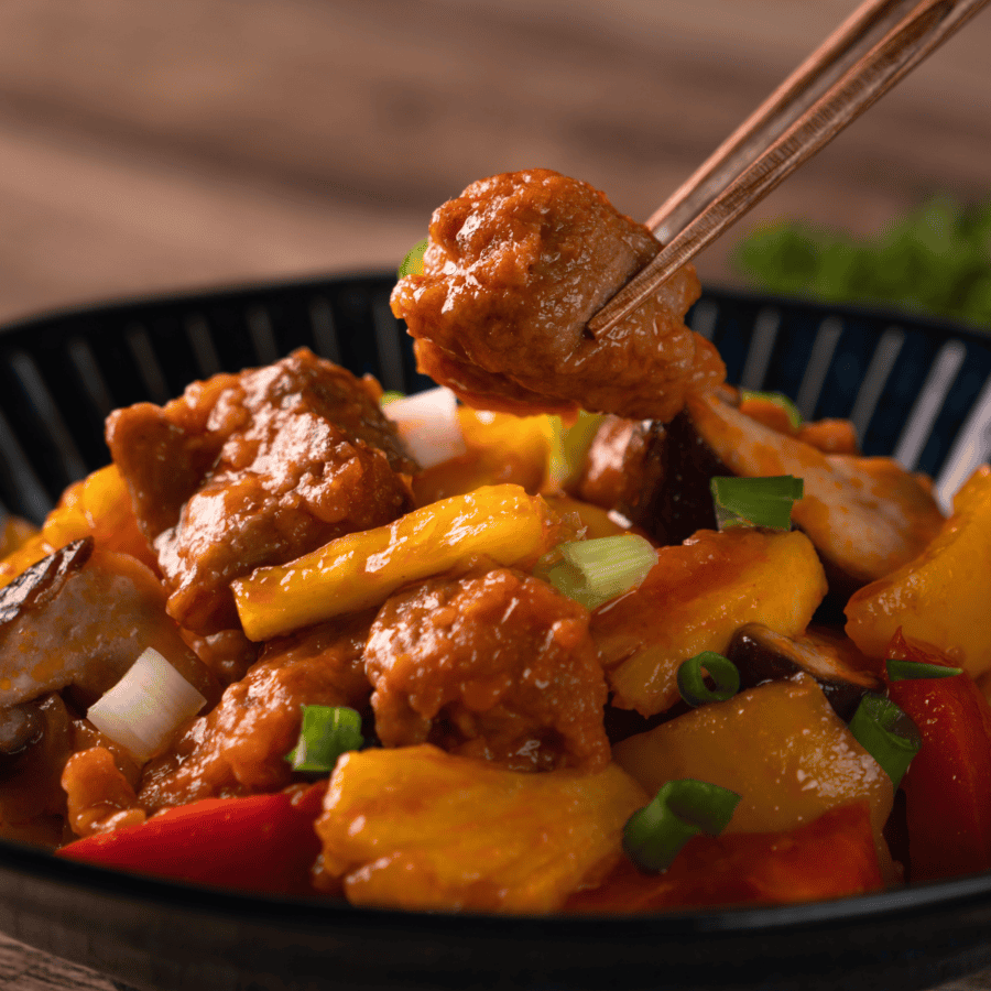 sweet and sour pork in a black bowl with chopsticks