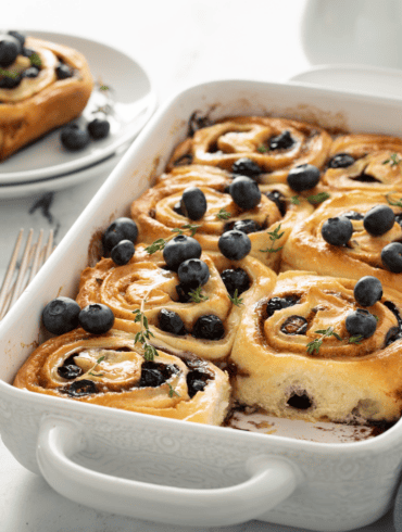 A white pan of blueberry cinnamon rolls with one taken out
