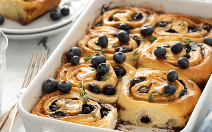 A white pan of blueberry cinnamon rolls with one taken out