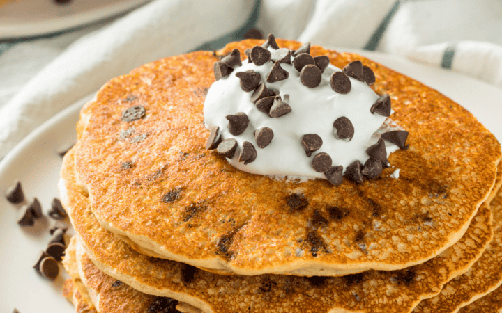 A stack of chocolate chip pancakes with whipped topping