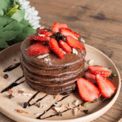 A stack of Chocolate Pancakes on a wooden plate with strawberry topping