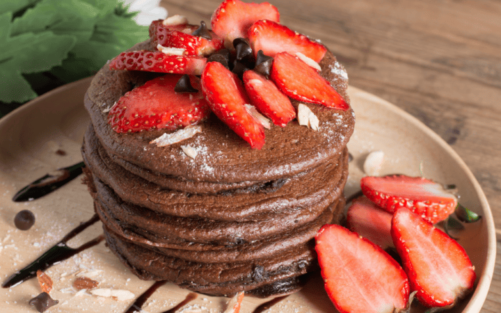 A stack of Chocolate Pancakes on a wooden plate with strawberry topping