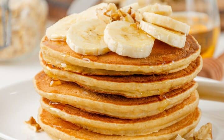 A Stack of Banana Oatmeal Pancakes on a white plate with fresh bananas on top