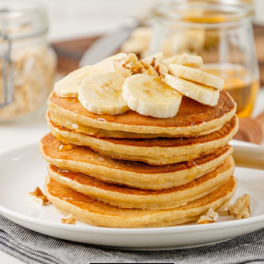 A Stack of Banana Oatmeal Pancakes on a white plate with fresh bananas on top