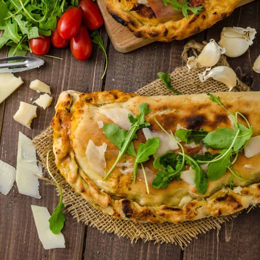 Close up image of a Calzone with cheese and fresh produce surrounding it