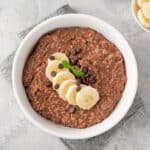 Overhead image of Chocolate Oatmeal in a white bowl with sliced bananas on top