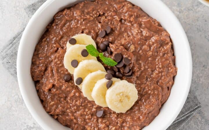 Overhead image of Chocolate Oatmeal in a white bowl with sliced bananas on top