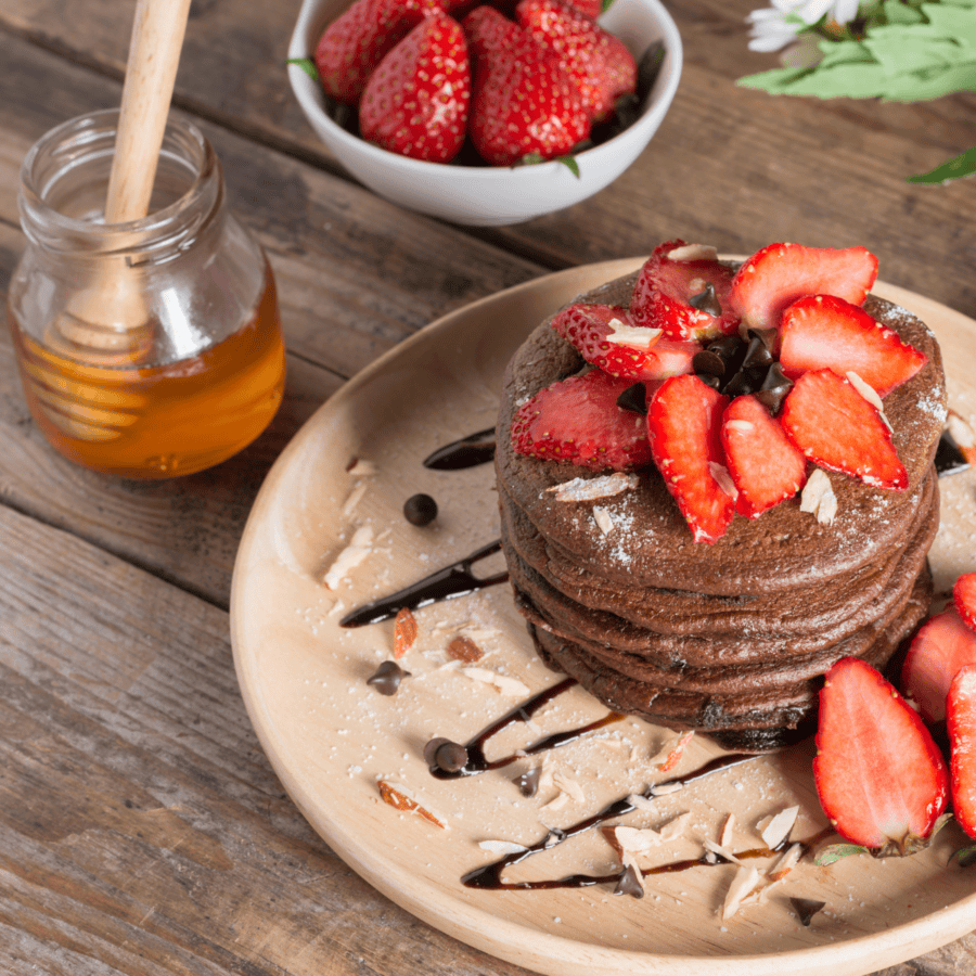 Overhead image of a stack of chocolate pancakes with strawberry topping on a wooden plate