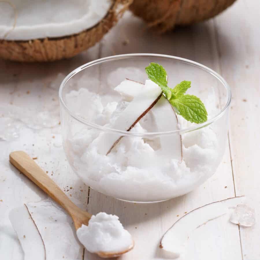 A glass bowl of coconut ice cream with two pieces of real coconut in the background