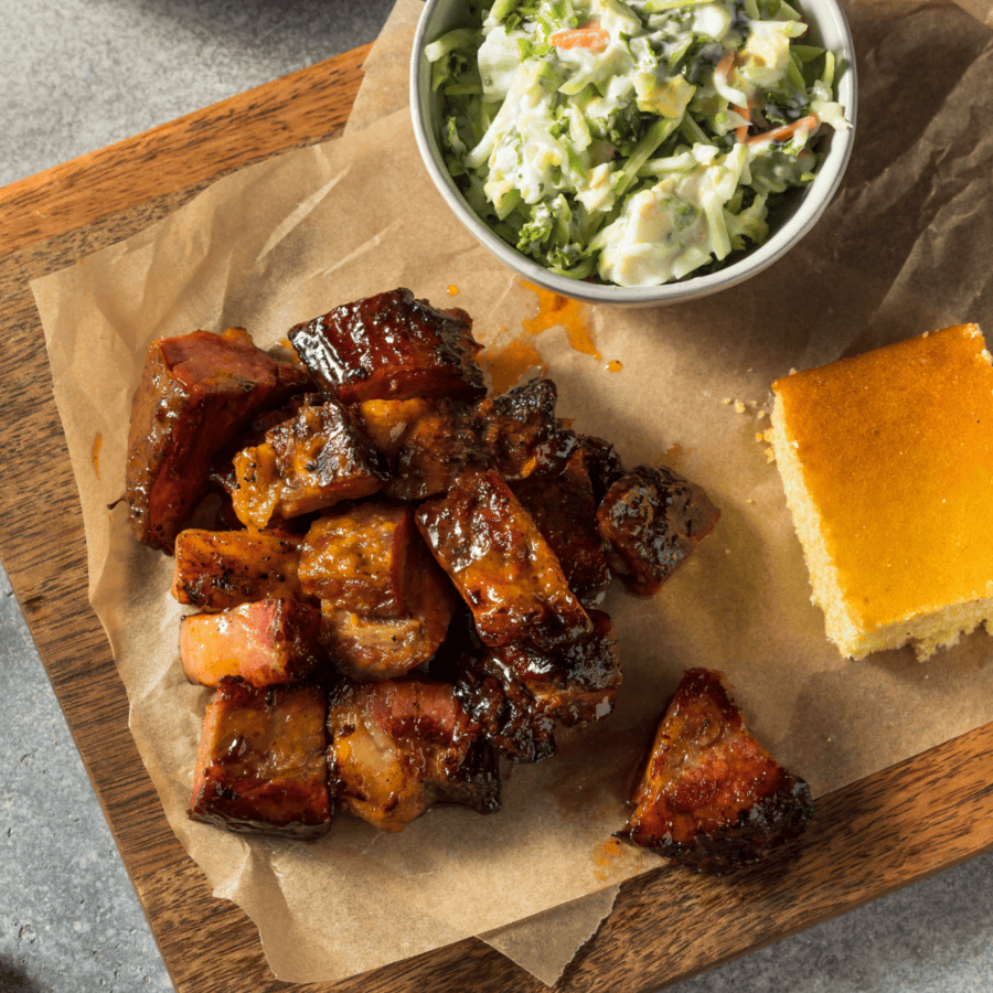 Overhead image of pork belly burnt ends on a wooden cutting board with traditional sides