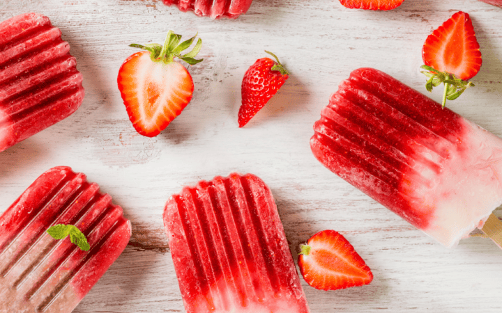 Overhead image of strawberry popsicles with sliced strawberries next to them