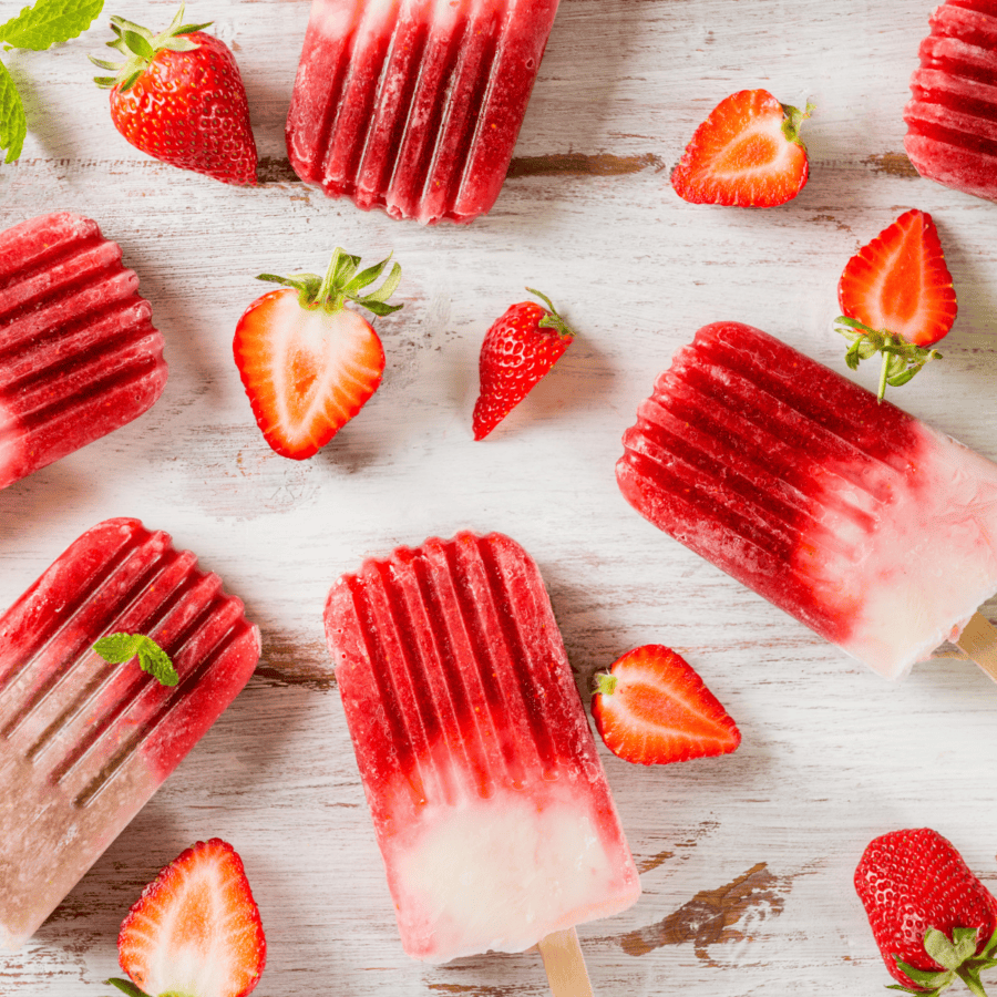 Overhead image of strawberry popsicles with sliced strawberries next to them