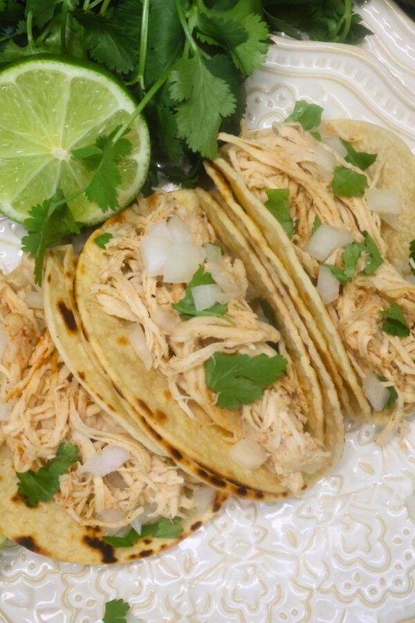 Overhead image of three slow cooker chicken street tacos on a white plate with cilantro and lime