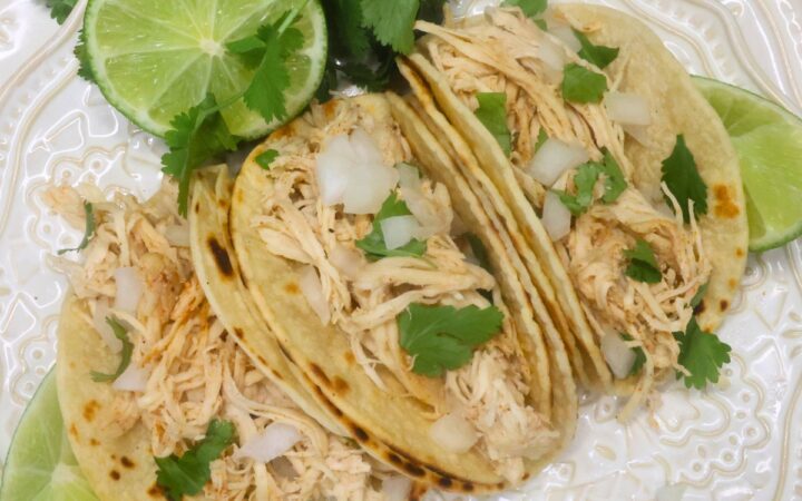 Overhead image of three slow cooker chicken street tacos on a white plate with cilantro and lime