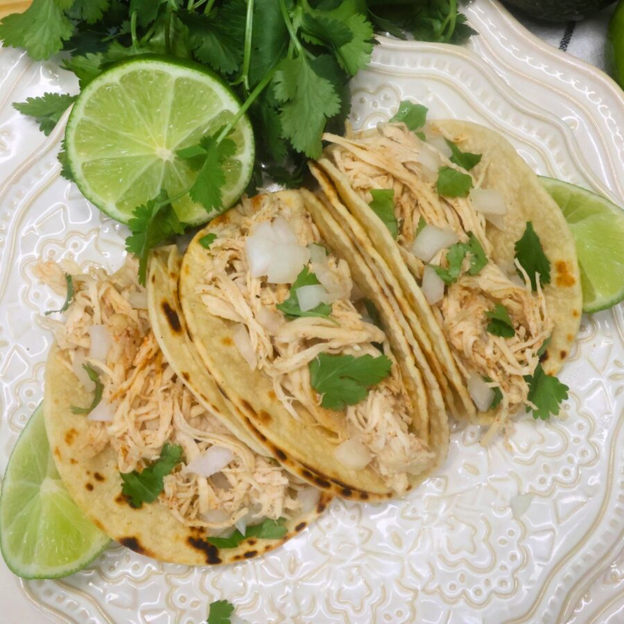 Overhead image of three slow cooker chicken street tacos on a white plate with cilantro and lime