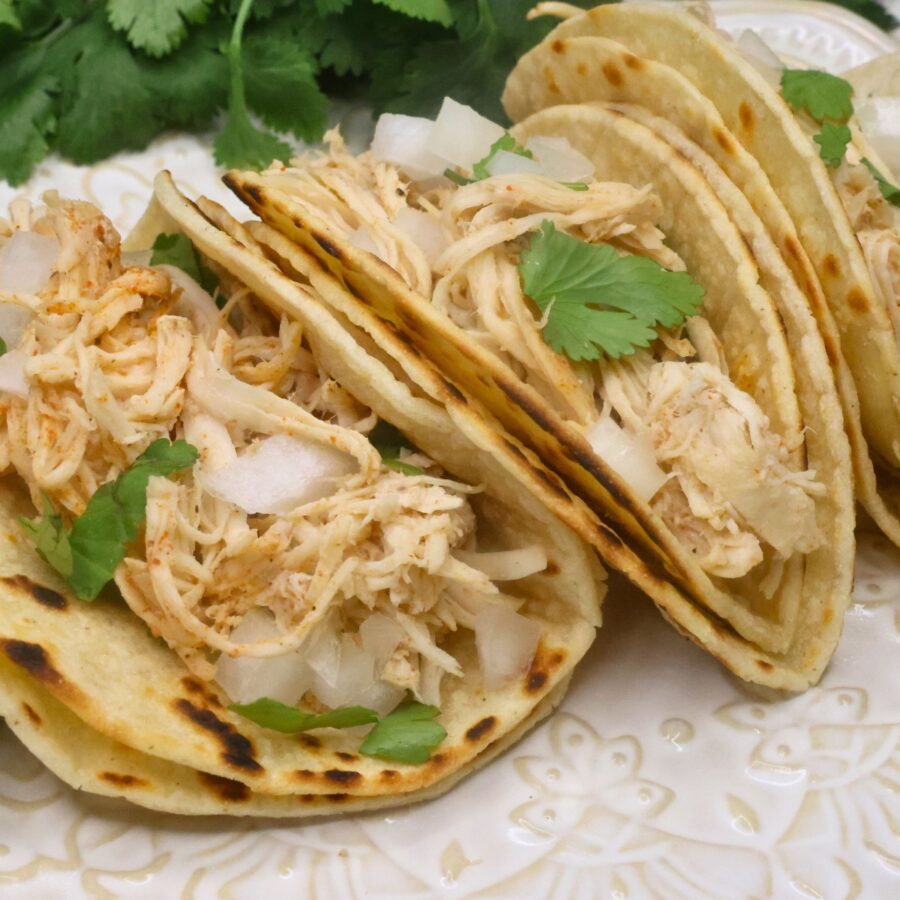 Close up image of three chicken street tacos with cilantro and chopped onion