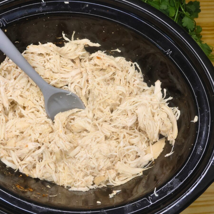 Shredded chicken breast for slow cooker chicken street tacos in a crockpot with a spoon in it