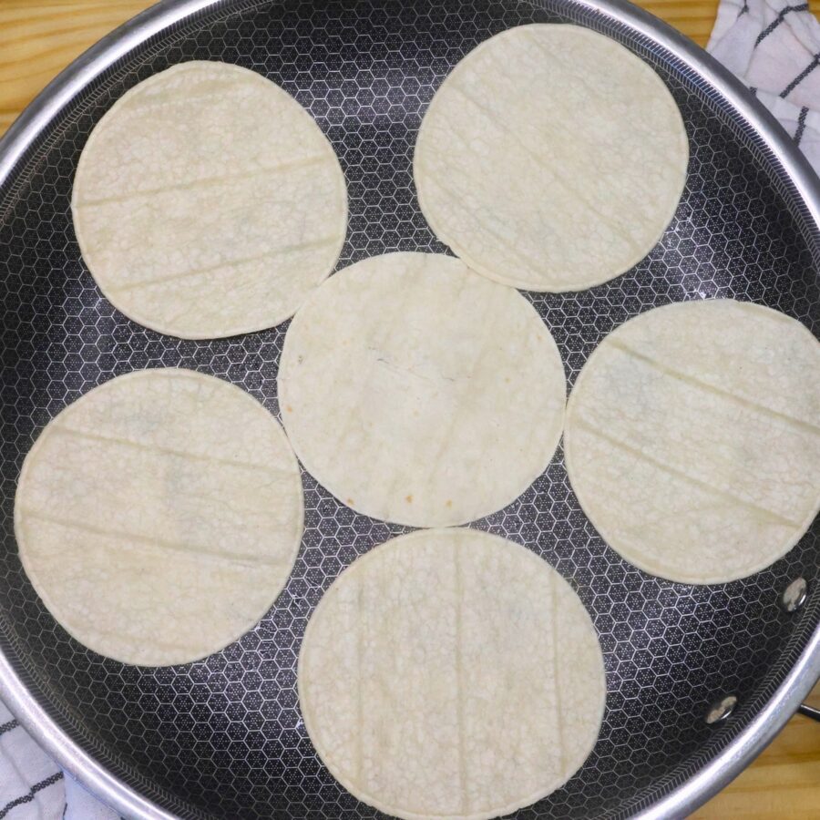 Six street taco sized corn tortillas in a skillet