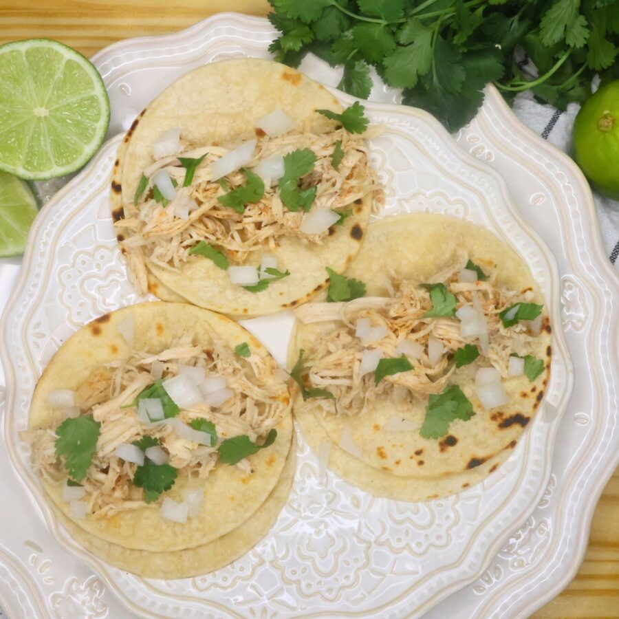 Overhead image of three slow cooker chicken tacos garnished with cilantro and chopped onion