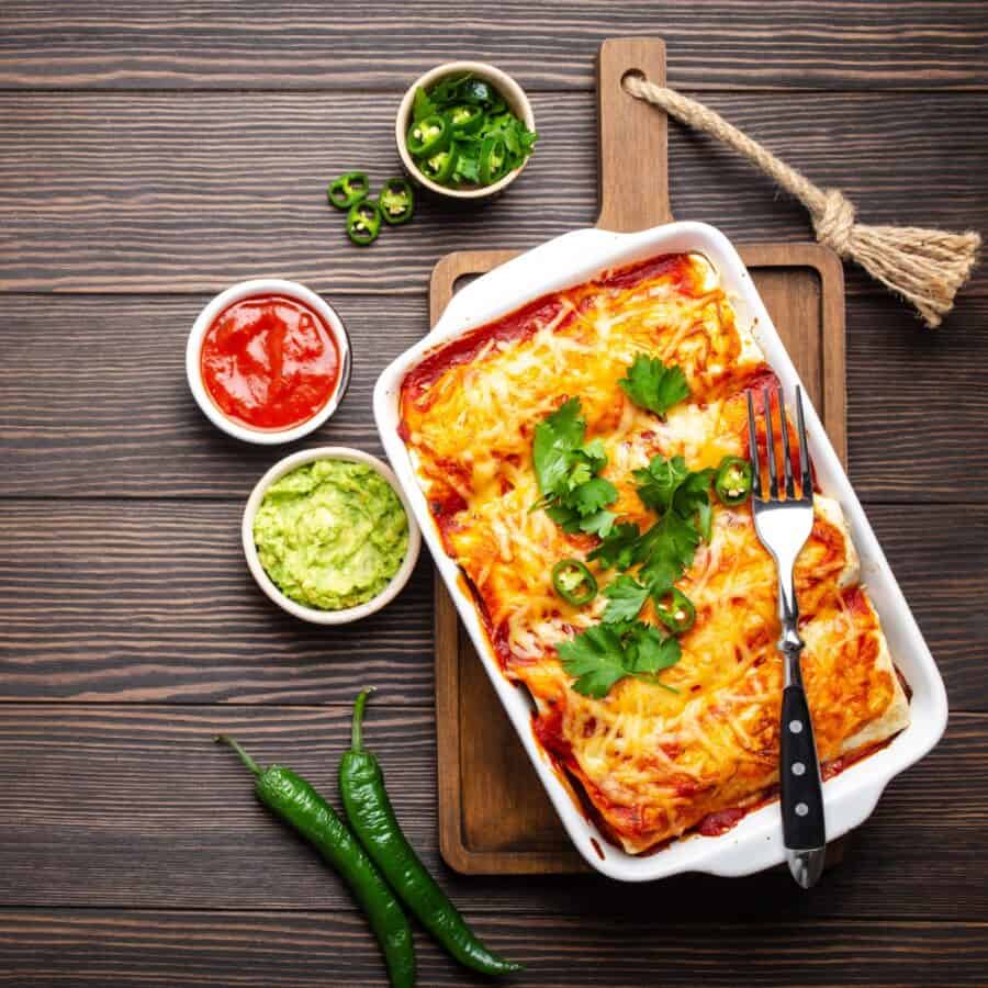 A pan of Beef and Been Enchiladas with garnishes in bowls surrounding it