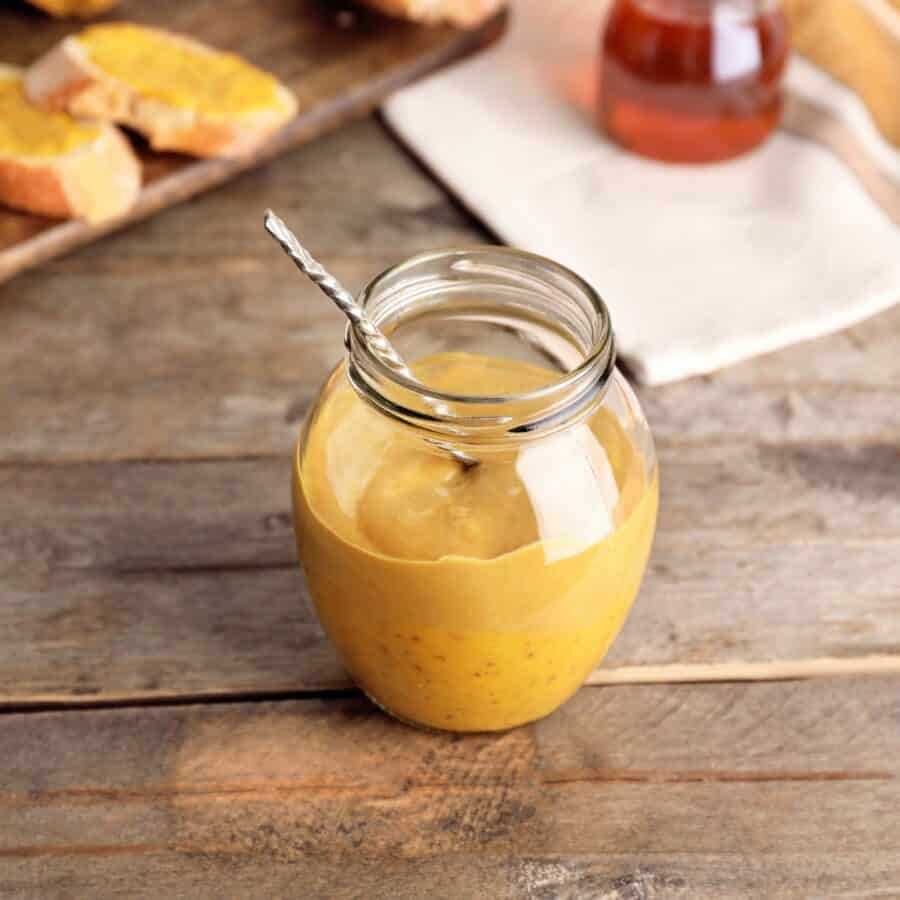 Overhead image of honey mustard sauce in a glass jar with ingredients to make it surrounding