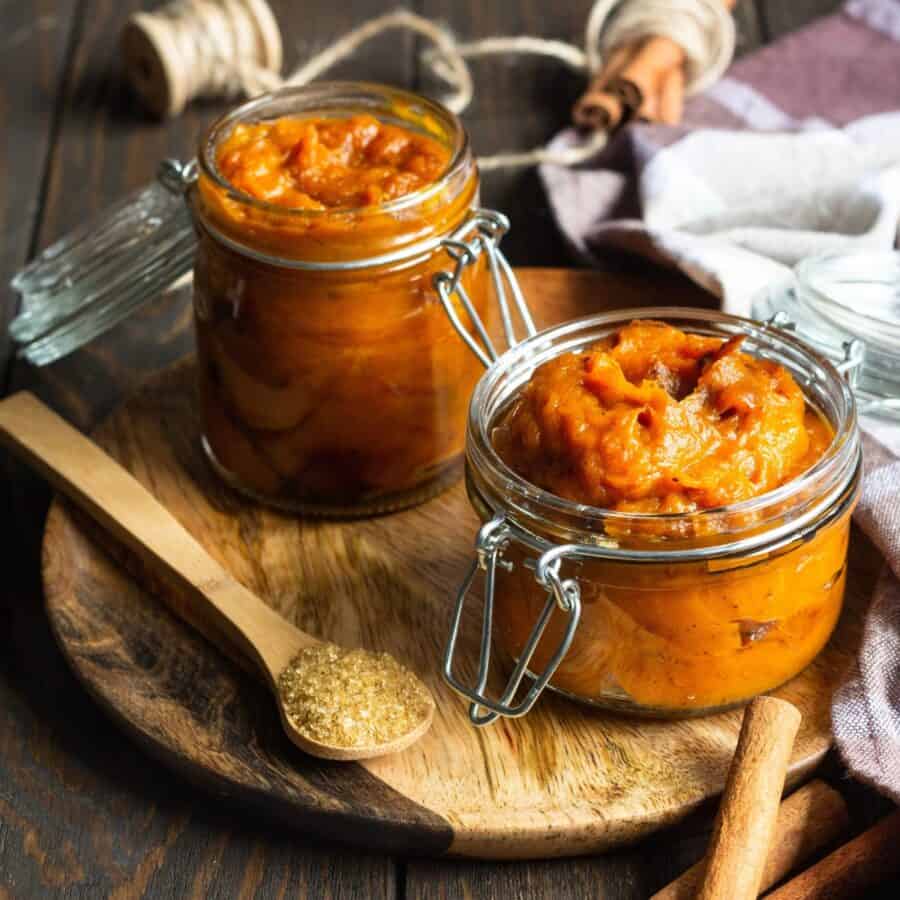 Two glass jars of Pumpkin Butter on a wooden cutting board