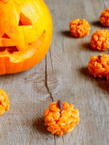 Pumpkin Rice Krispies Treats on a wooden table with a jackolantern in the background