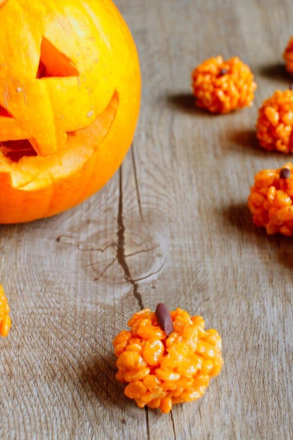 Pumpkin Rice Krispies Treats on a wooden table with a jackolantern in the background