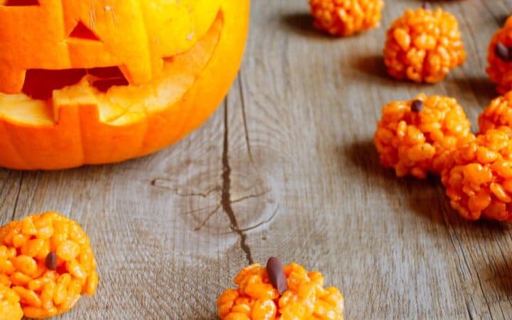 Pumpkin Rice Krispies Treats on a wooden table with a jackolantern in the background