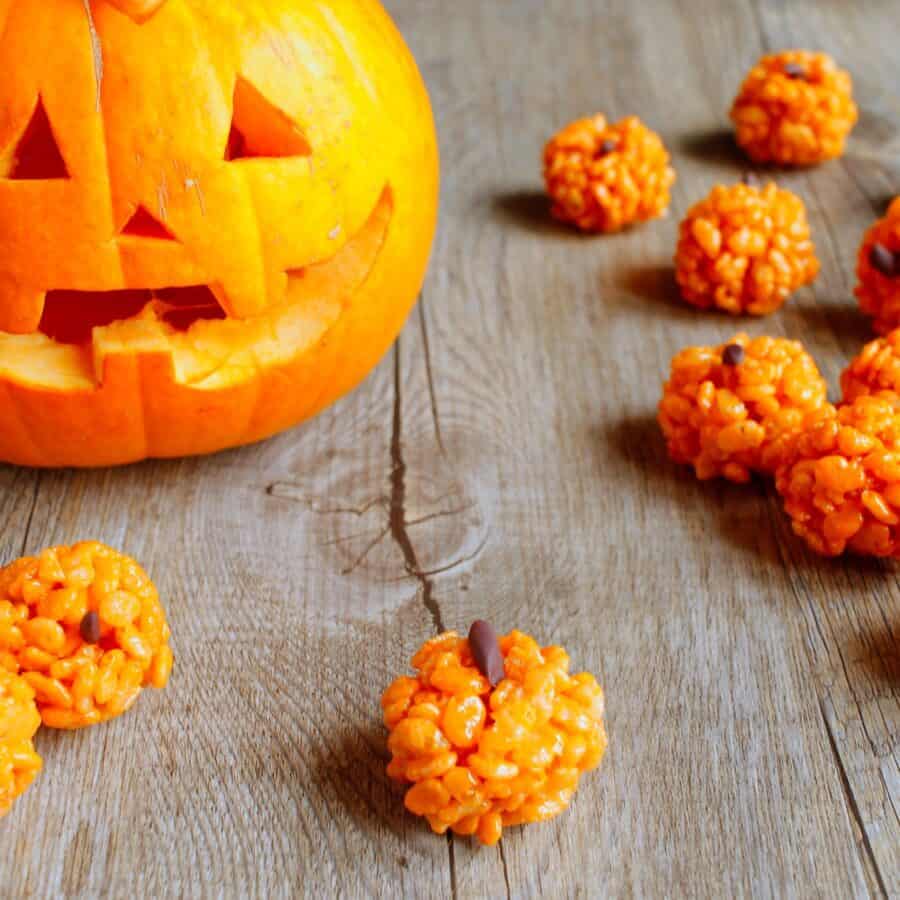 Pumpkin Rice Krispies Treats on a wooden table with a jackolantern in the background