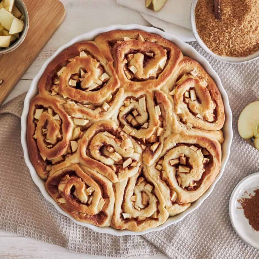 Overhead image of Apple Cinnamon Rolls in a round baking dish with ingredients surrounding it