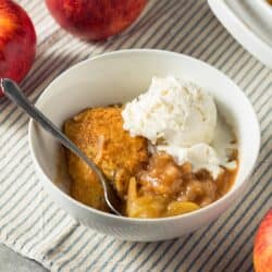 A white bowl full of Apple Cobbler and a scoop of vanilla ice cream