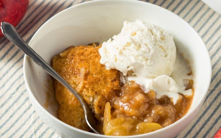 A white bowl full of Apple Cobbler and a scoop of vanilla ice cream