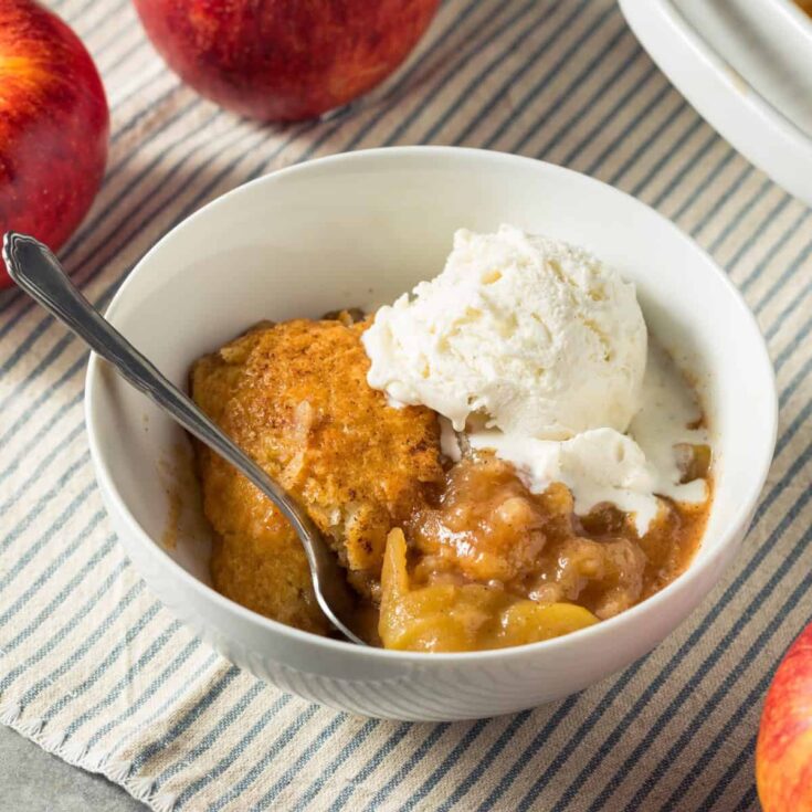 A white bowl full of Apple Cobbler and a scoop of vanilla ice cream