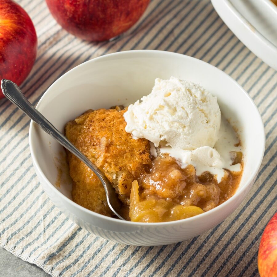 A white bowl full of Apple Cobbler and a scoop of vanilla ice cream