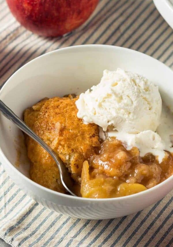 A white bowl full of Apple Cobbler and a scoop of vanilla ice cream